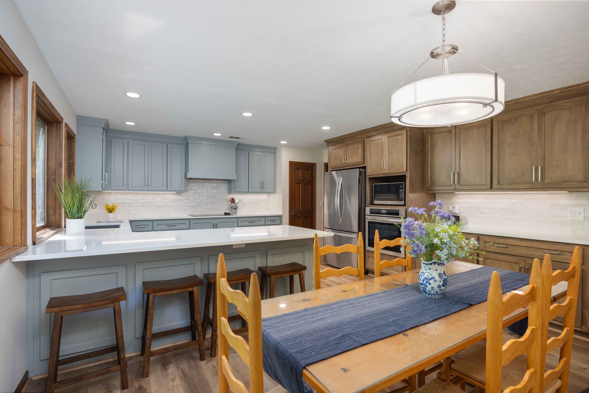 Bright kitchen and dining area with wood cabinets, island stools, and a table set with flowers.