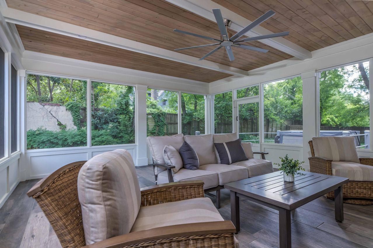Bright screened porch with wicker and cushioned seating, coffee table, wood ceiling, and ceiling fan.