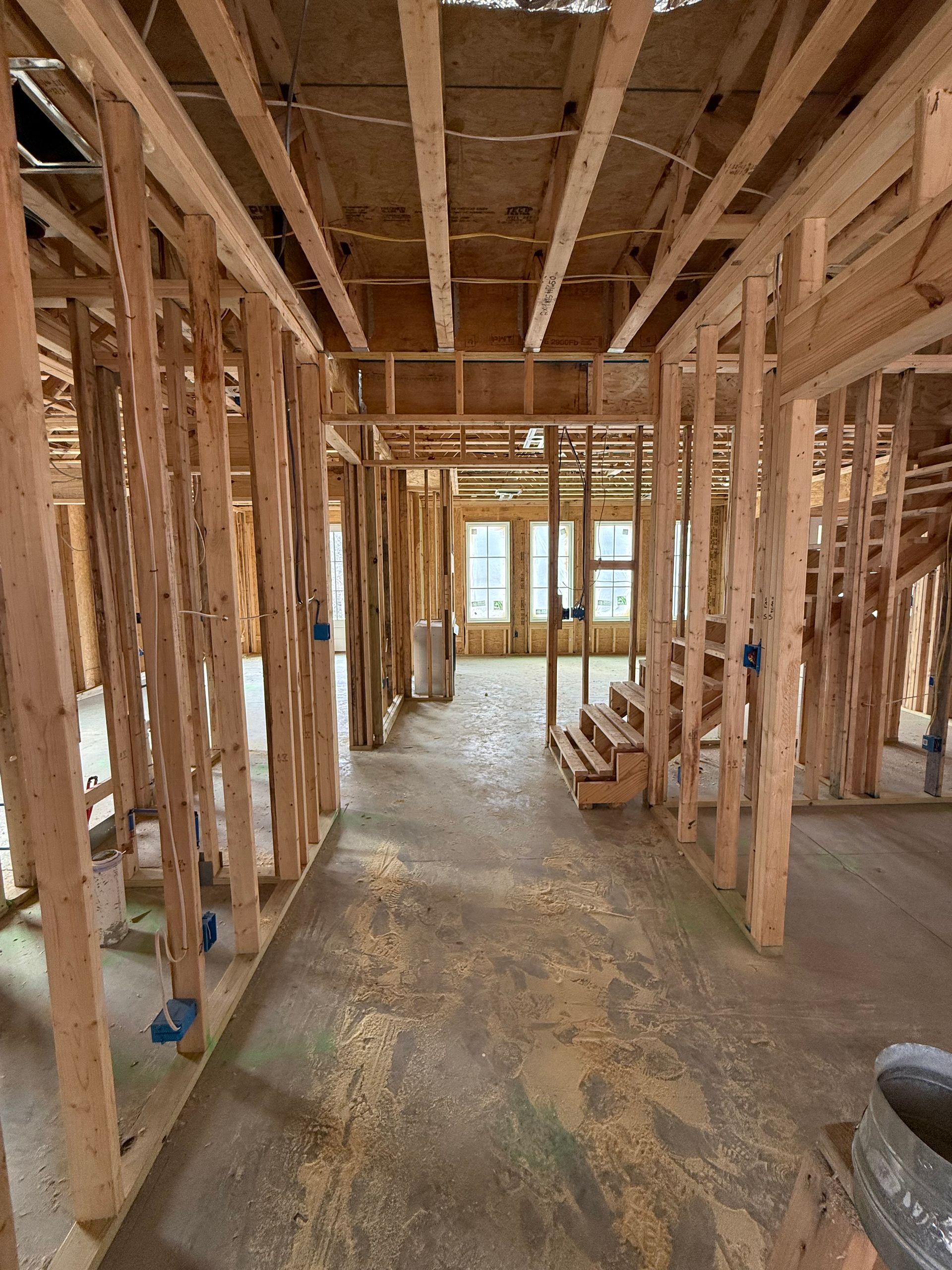 Interior of a house under construction with exposed wooden framing and stairs down the hallway