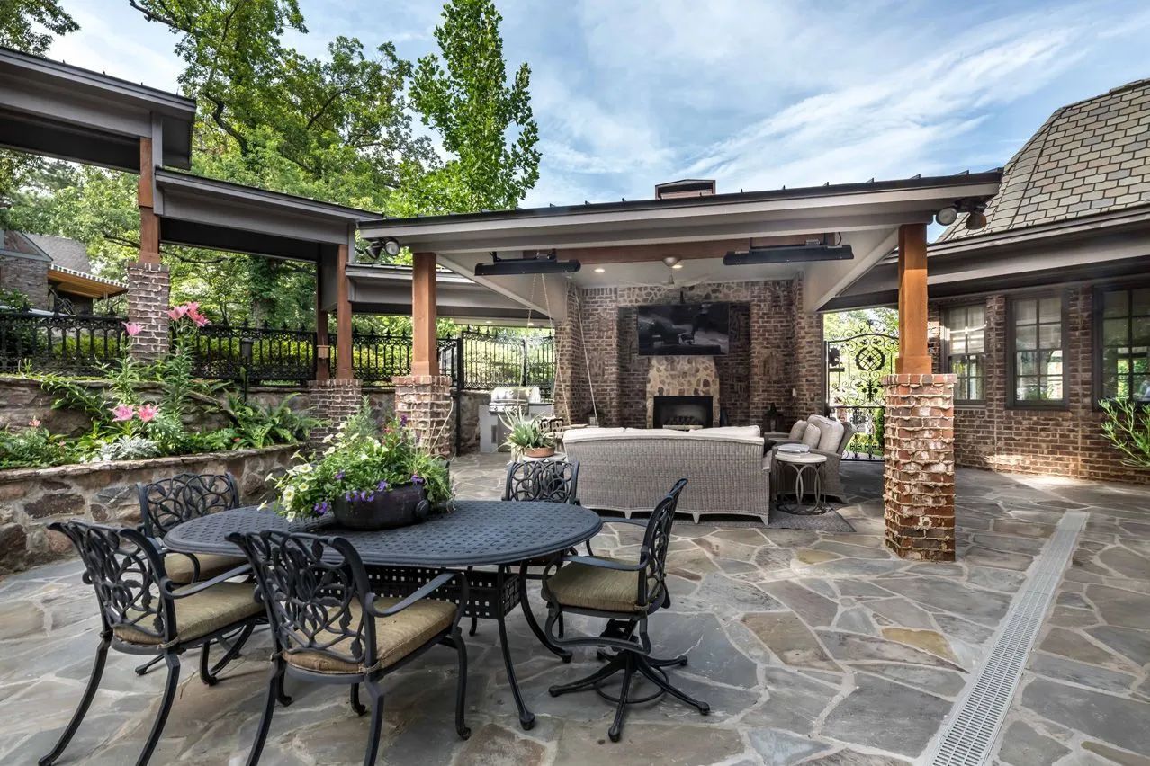 Stone-patio outdoor seating area with dining table, chairs, and covered lounge under a pergola