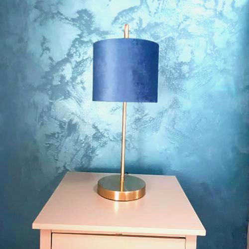 Blue wall with plastered effect. Stand with blue and gold lamp.