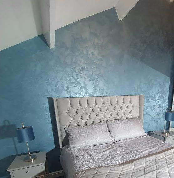 Stylish bedroom with light grey bed against light blue wall with textured plaster finish
