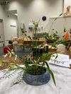Bloemstuk in een blauwe, gestructureerde pot op een tafel. Groen en witte bloemen strekken zich naar buiten uit. Studio-omgeving.