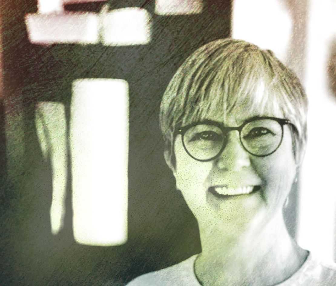 Vrouw met kort haar, een ronde bril en een glimlachende uitdrukking.
