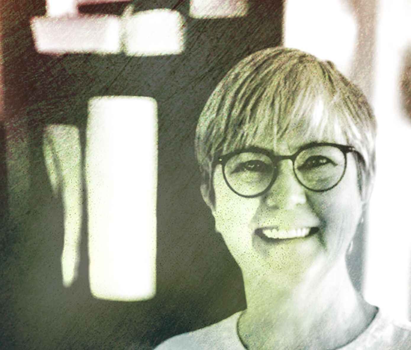 Vrouw met kort haar, een ronde bril en een glimlachende uitdrukking.