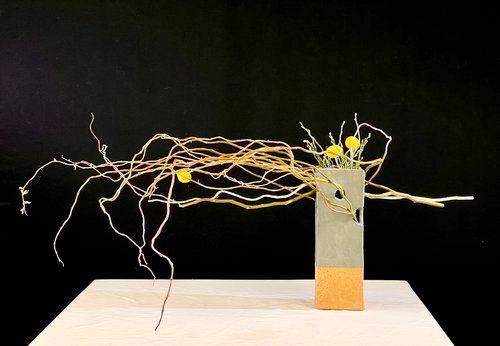 Bloemstuk met gele bloemen en gedraaide takken in een moderne, rechthoekige vaas.