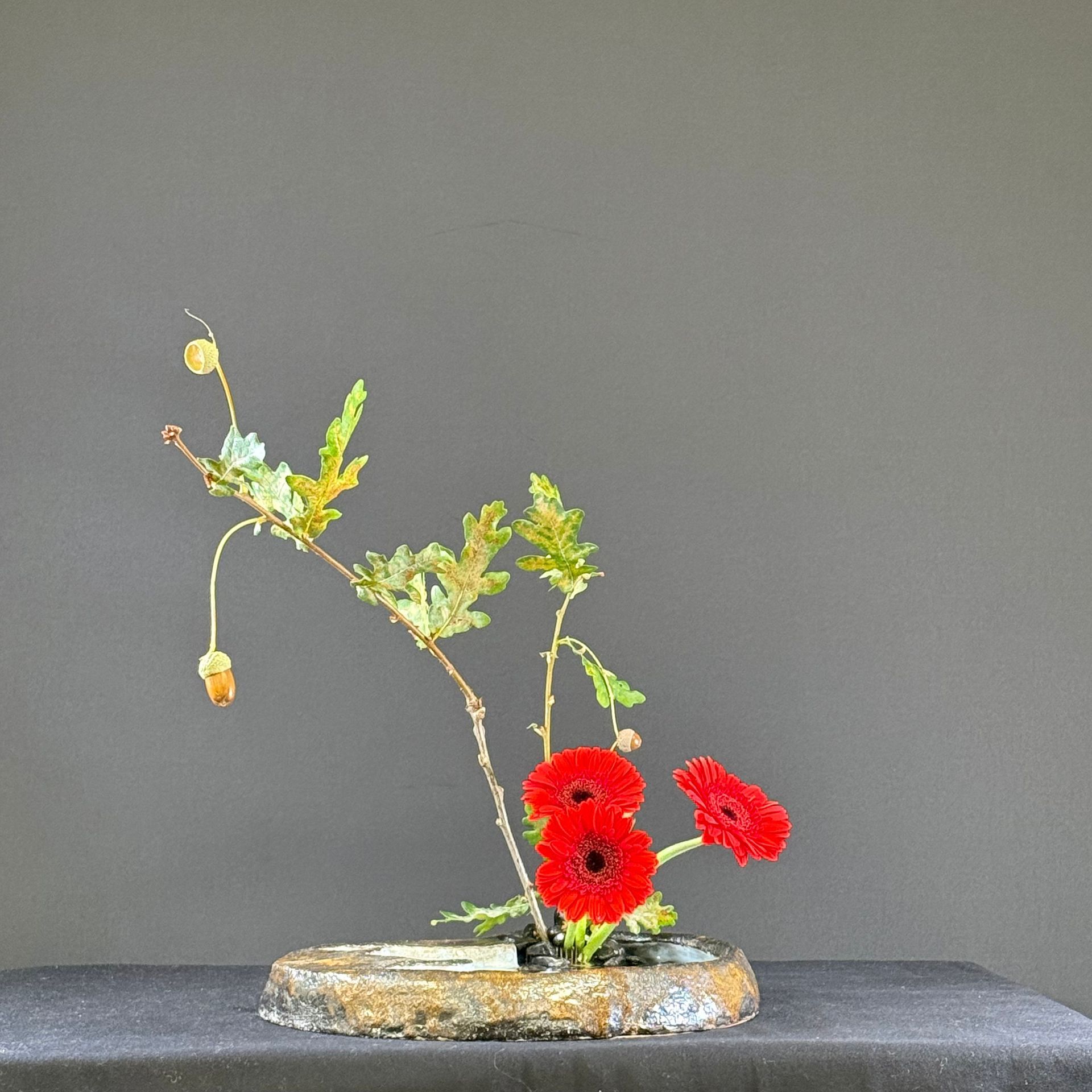 Bloemstuk met rode bloemen en groen blad in een donkere vaas.