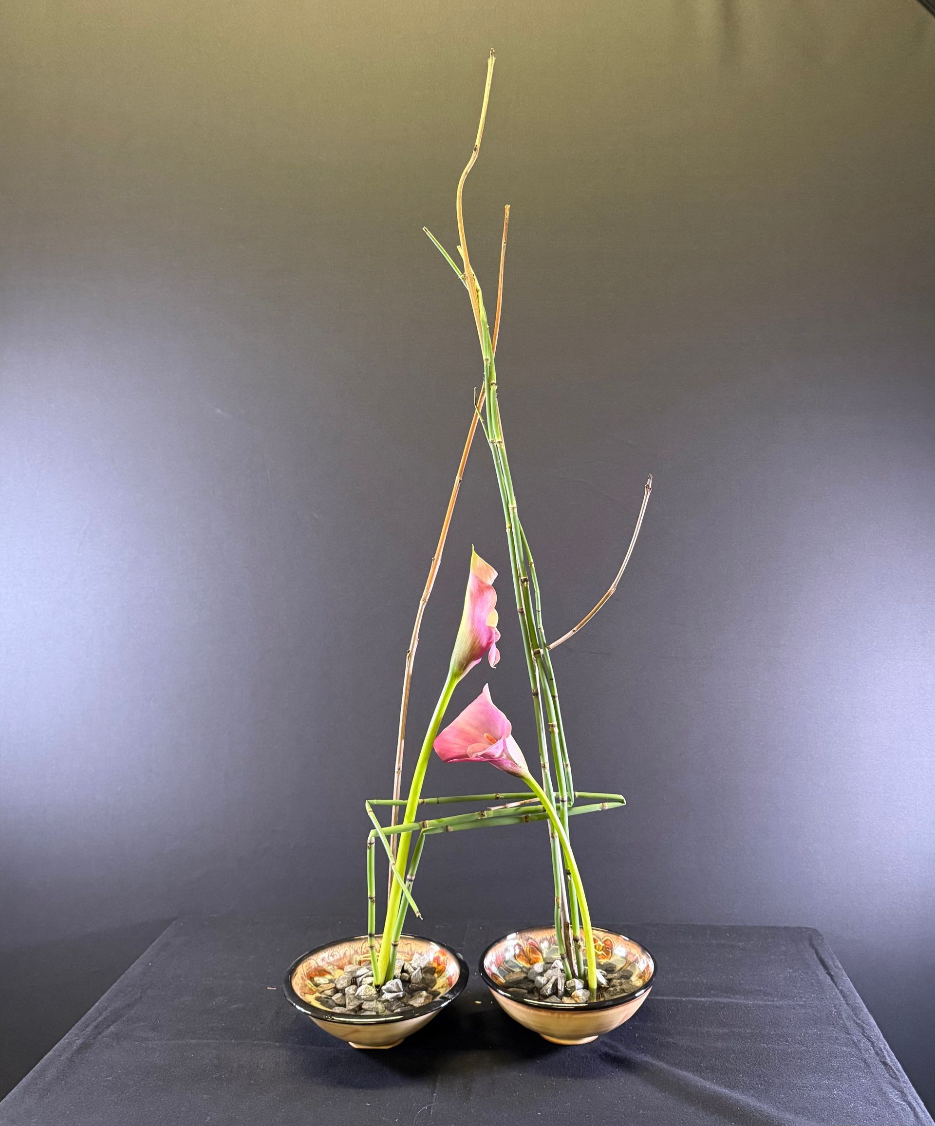 Bloemstuk: Twee kleine schalen met roze bloemen en lange groene stelen, die samen een 