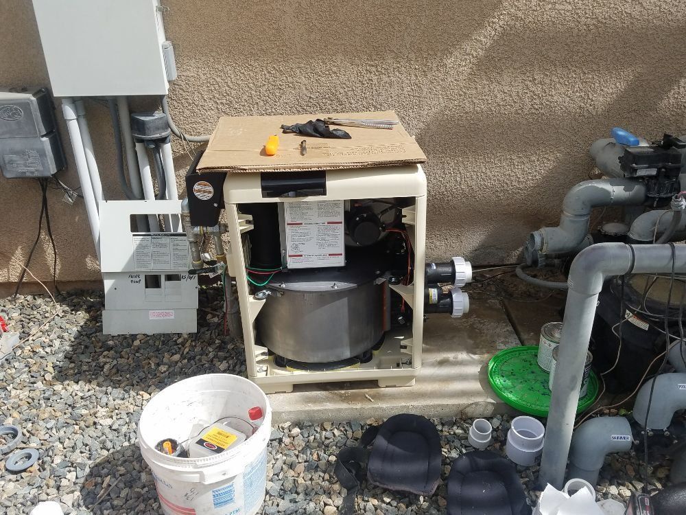 Outdoor pool equipment cabinet with pump, pipes, bucket, and tools on gravel рядом with a wall