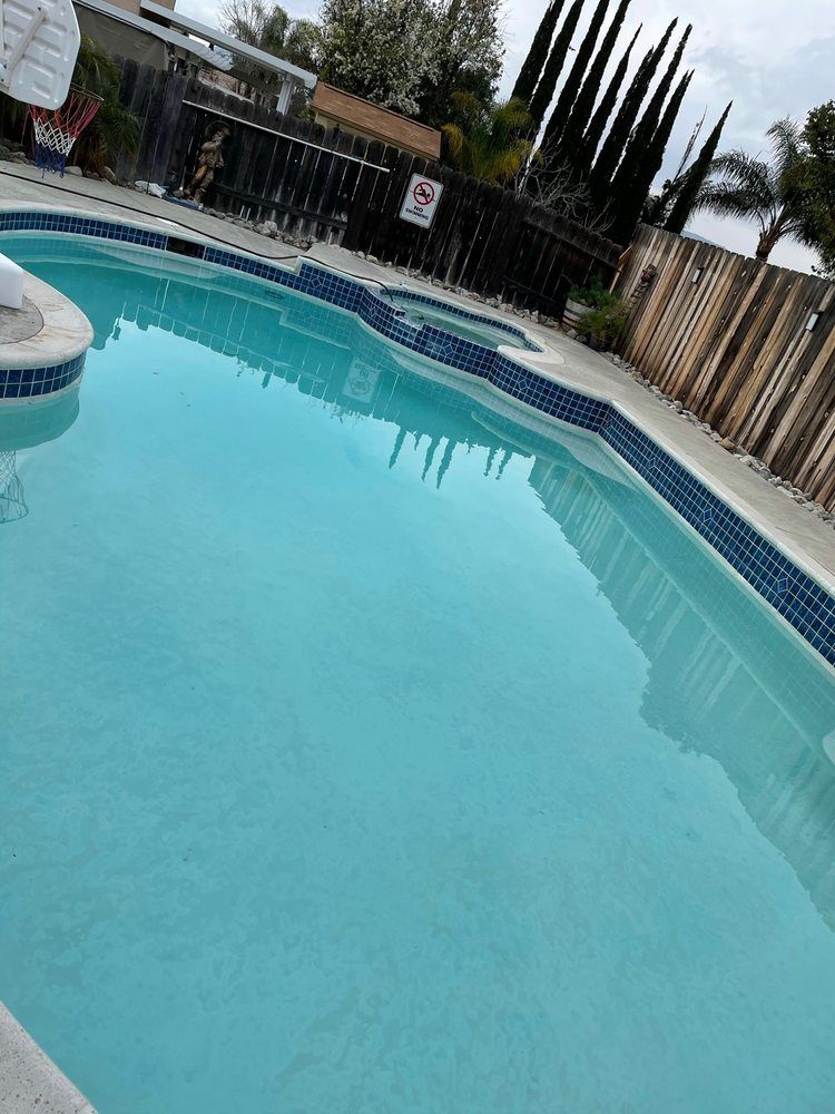 Backyard swimming pool with clear blue water, tile border, and fence surrounding it