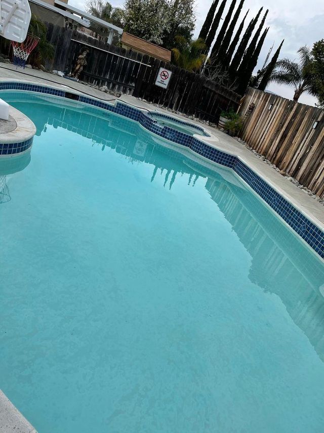 Backyard swimming pool with turquoise water, blue tile border, and a fenced patio area