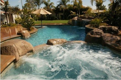 Resort pool with waterfall, hot tub, palm trees, and lounge chairs in a tropical setting