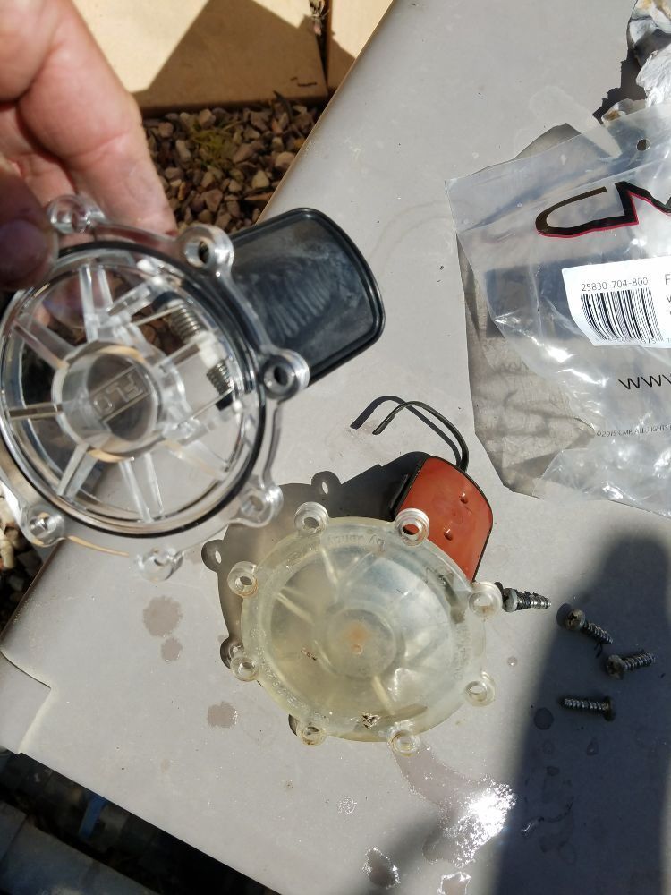 Two small clear plastic pump parts on a workbench, one held by a hand.