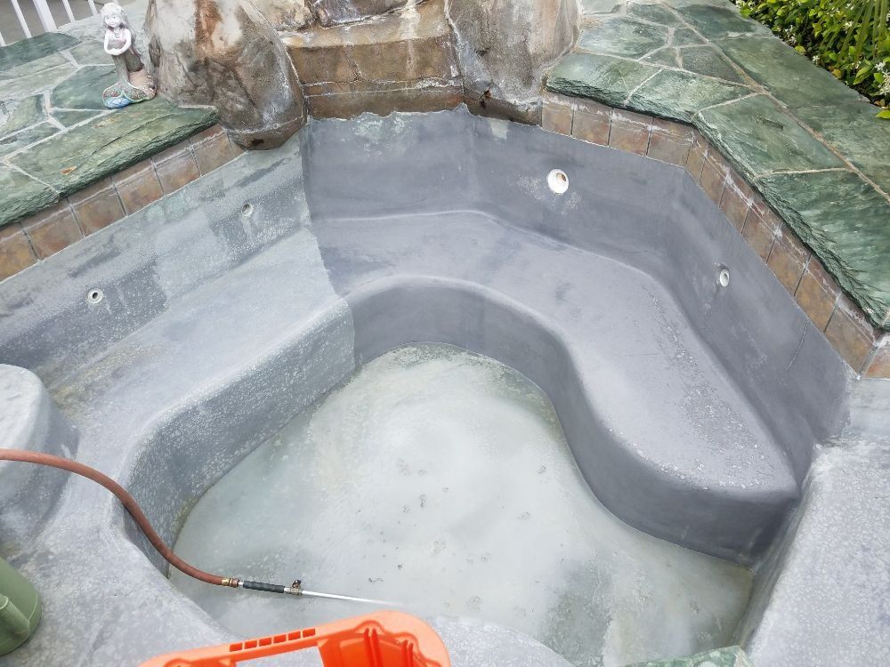 Empty gray hot tub with built-in steps and green tile edging, viewed from above