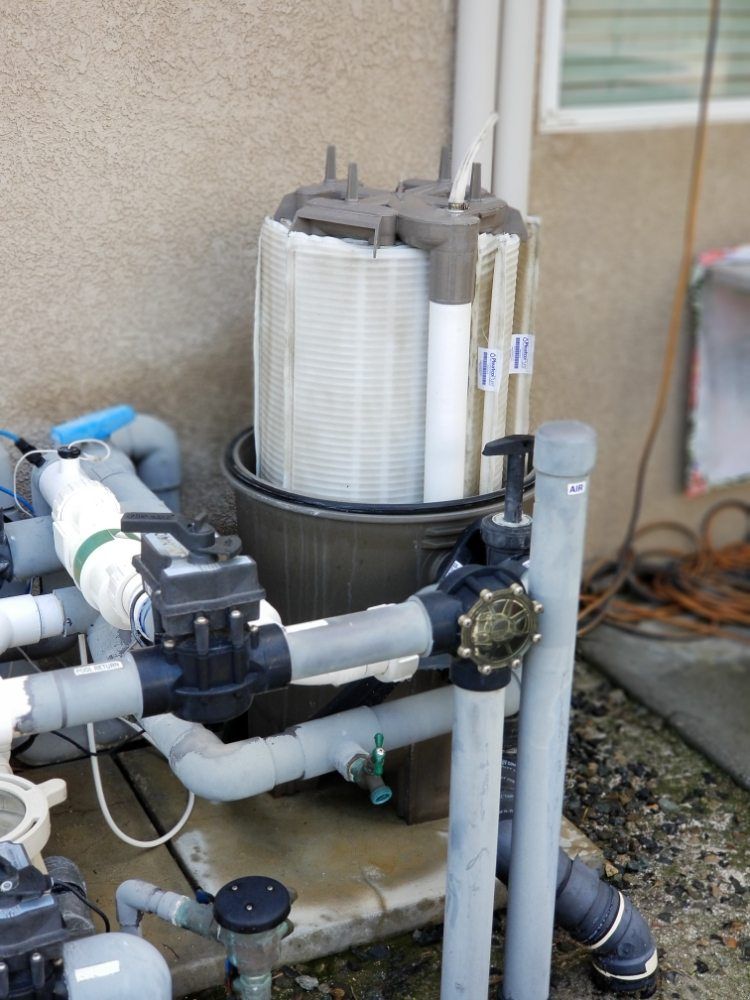 Outdoor pool pump and filtration system with white pipes and black motor beside a house wall