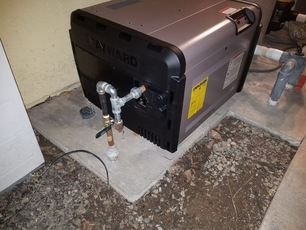 Metal furnace unit in a basement with exposed pipes and a wall-mounted gas valve.
