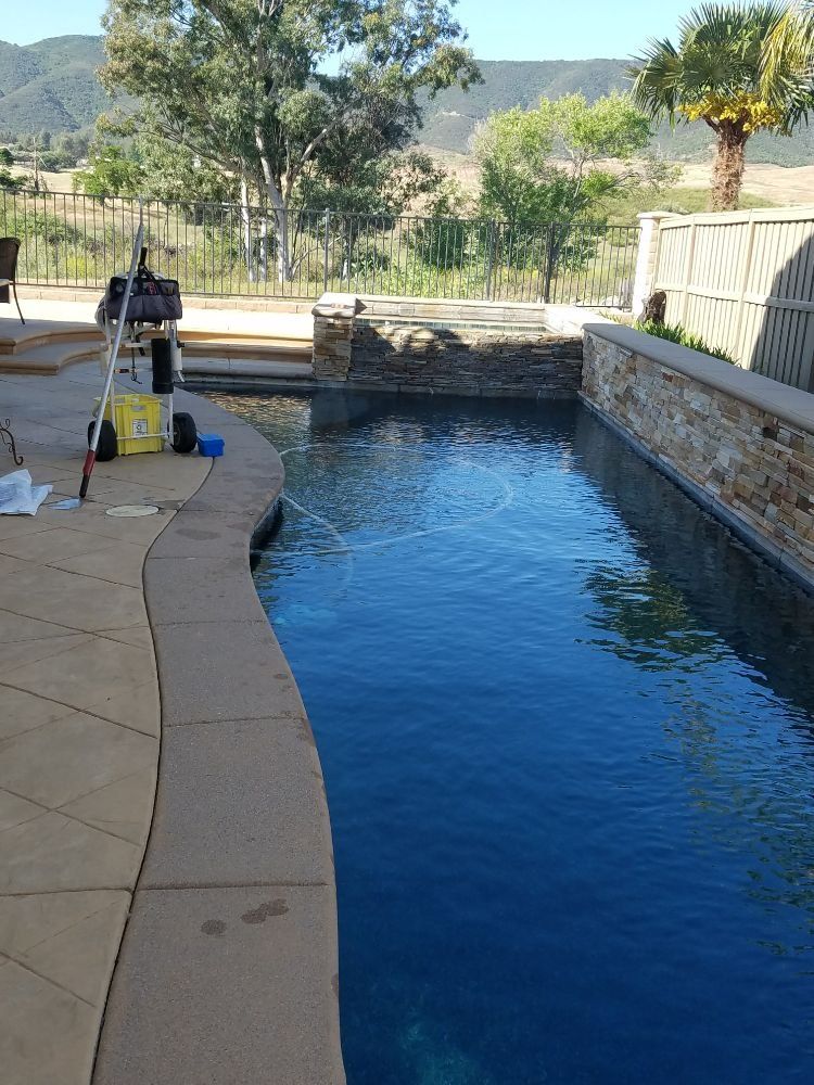 Backyard pool with blue water, stone patio, and landscaping with hills in the background