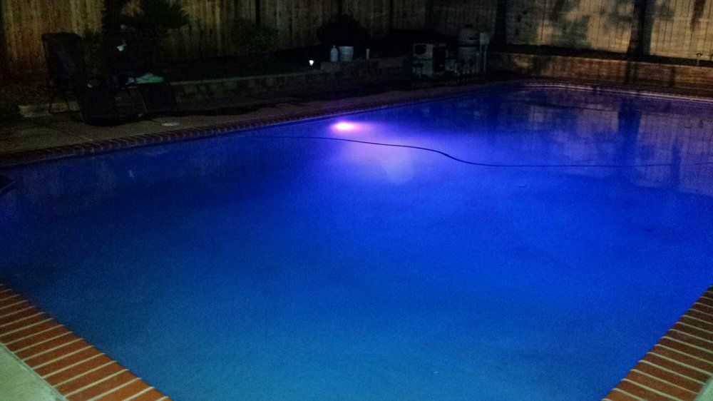 Blue-lit swimming pool at night with a bright purple light reflecting on the water.