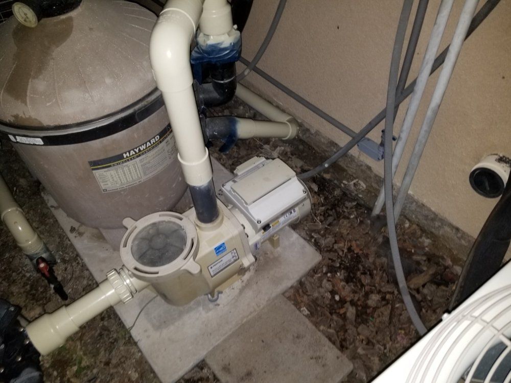 Pool pump and filter equipment in a utility area with pipes, wires, and debris on the floor