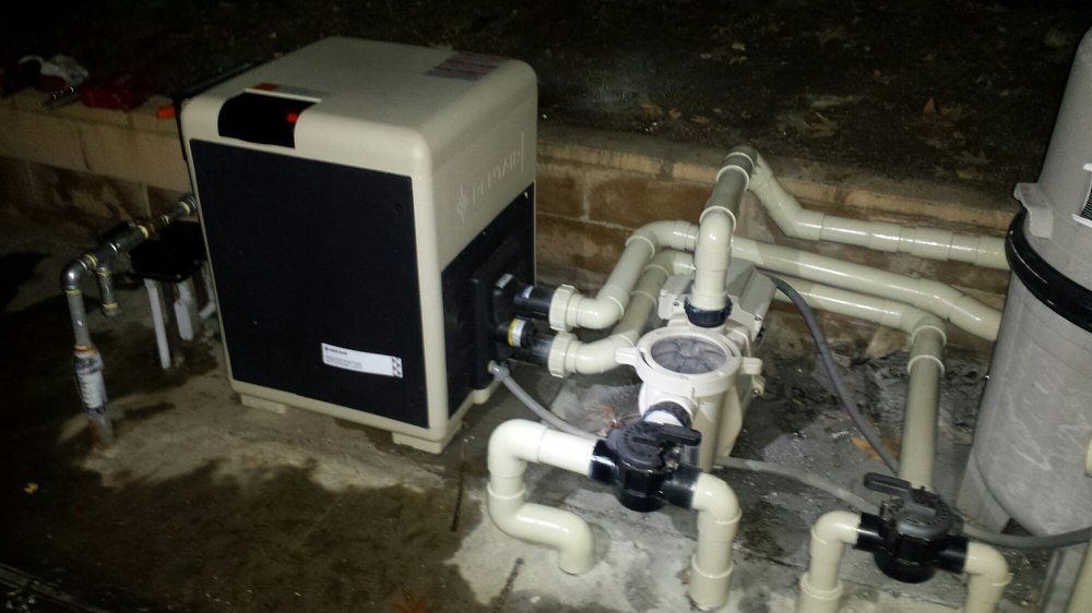 Pool pump and filtration equipment with white pipes and a black unit in a dim utility area