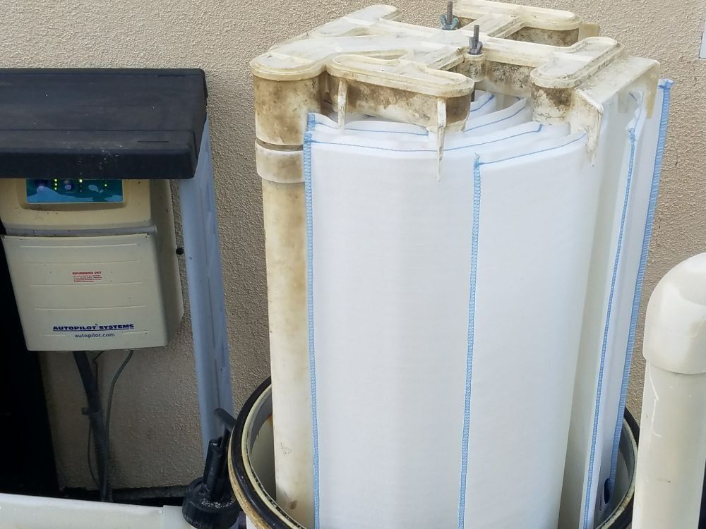 White cylindrical tank with wrapped insulation beside a small black-and-white appliance in a utility area