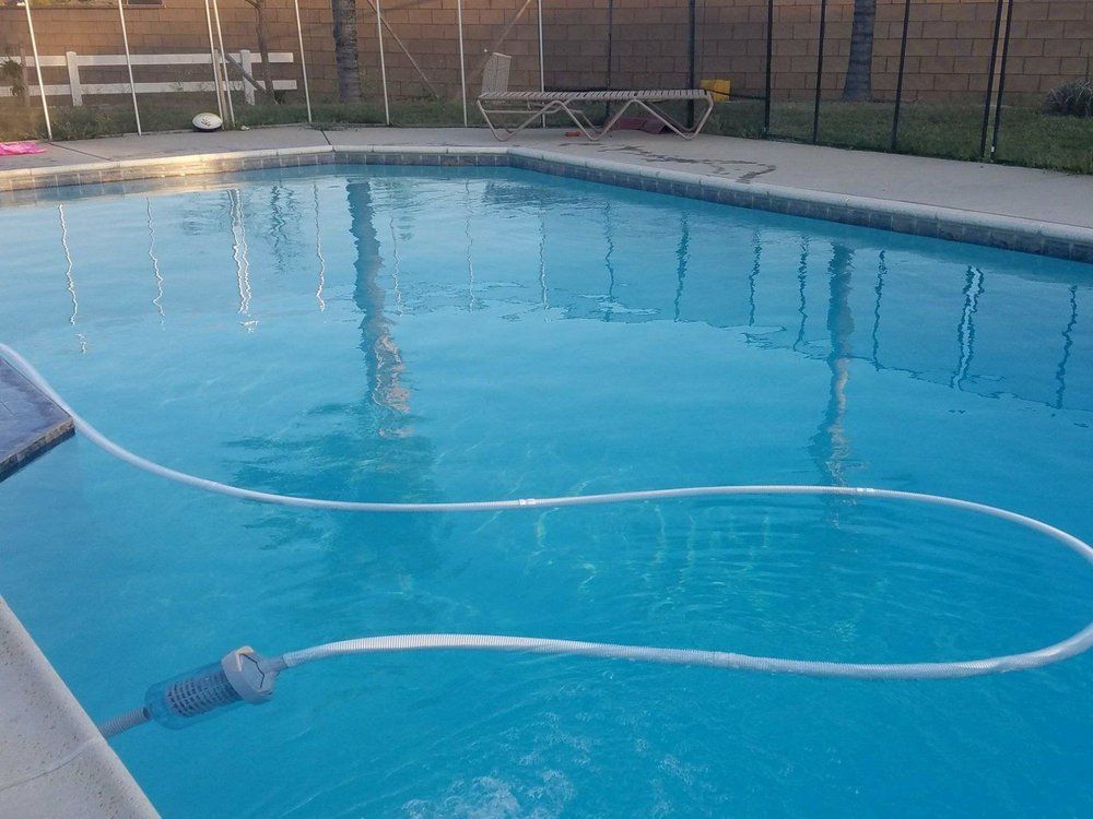 Blue swimming pool with a hose floating across the water and a pool deck in the background