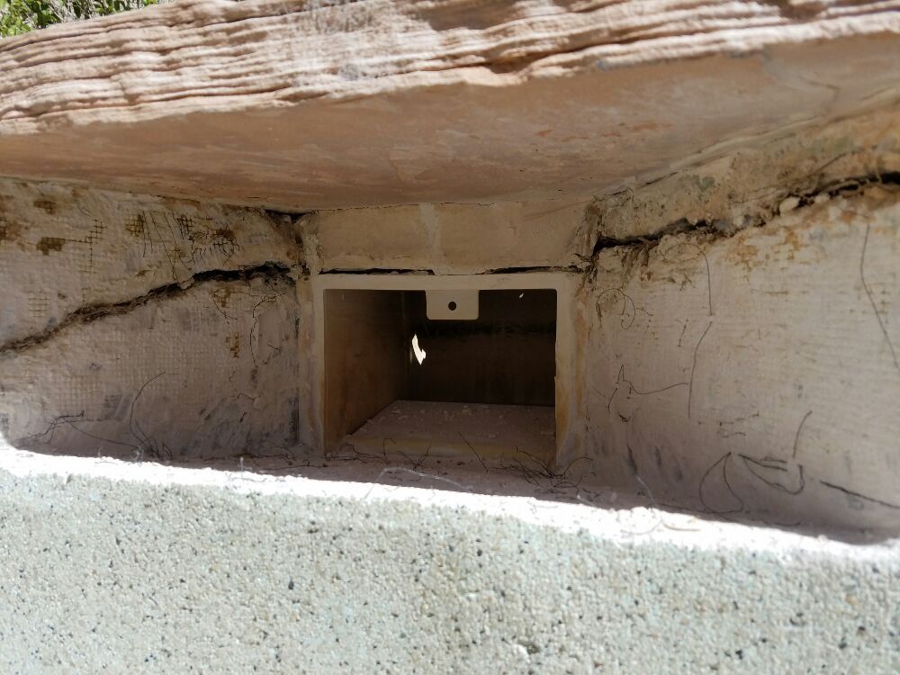 Stone cave entrance with a narrow dark opening beneath a low rock overhang.