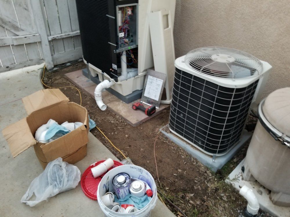Outdoor HVAC area with an open air conditioner, hoses, boxes, and cleaning supplies on the ground