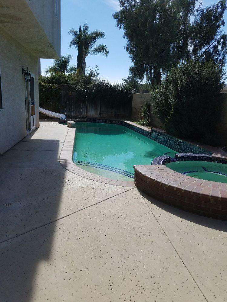 Backyard pool with turquoise water, concrete patio, and a small circular hot tub under palm trees.