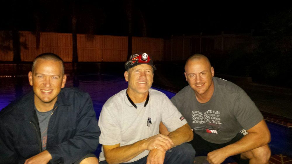 Three smiling men sitting close together in a dimly lit bar or lounge.