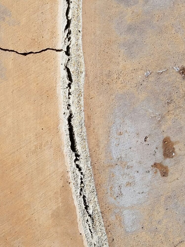 Close-up of a cracked beige wall with a vertical jagged fissure and a small horizontal crack on the left.