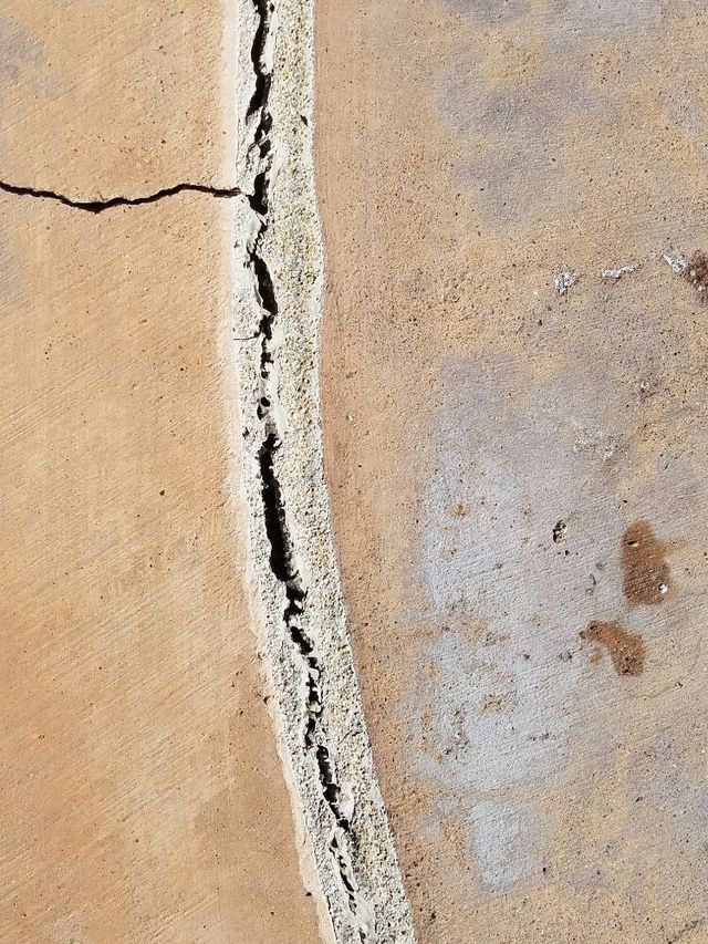 Close-up of a cracked beige wall with a vertical gap and peeling white sealant.