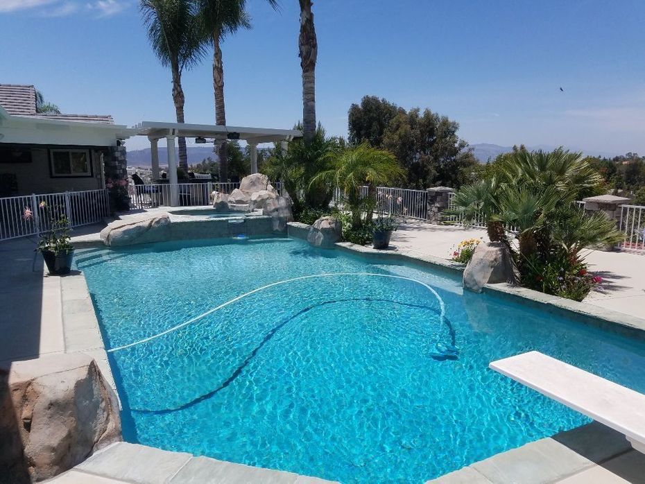 Backyard pool with turquoise water, palm trees, rocks, and a white diving board under a clear sky