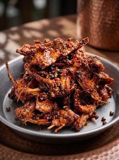 A plate of glossy, spicy-looking fried meat or mushrooms piled on a gray dish.