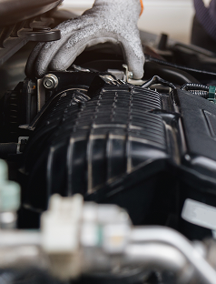 Gloved hands working on a car engine bay, with black plastic components and metal parts visible. | Walt Eger's Service Center