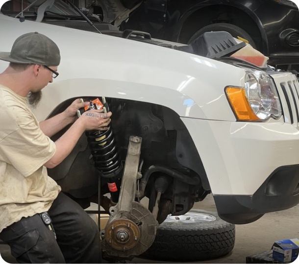 Person working on a white SUV’s front suspension in a garage, with the wheel removed. | Walt Eger's Service
