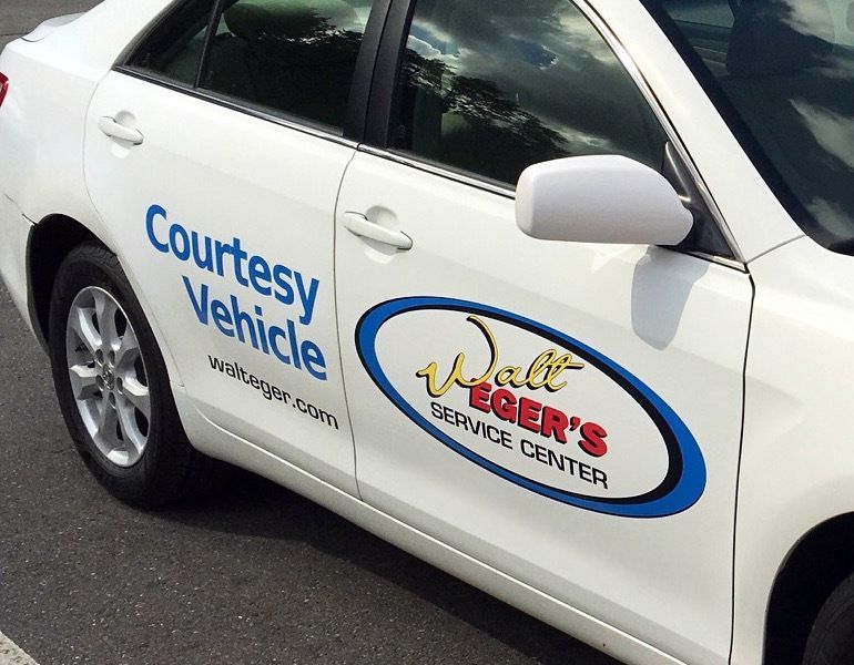 White courtesy vehicle with car dealership logos on the side, parked outdoors. | Walt Eger's Service Center