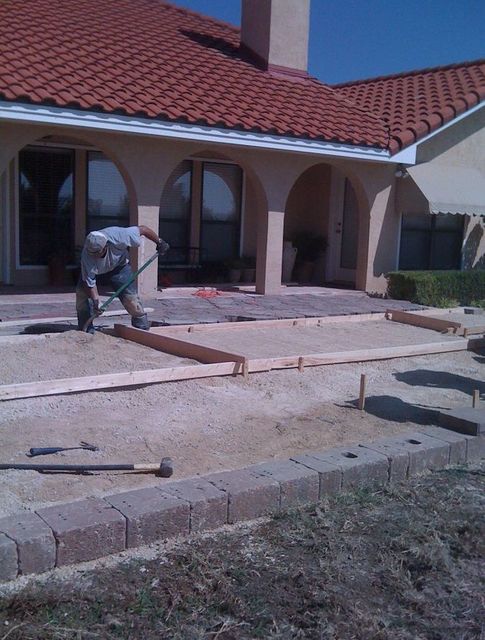 A man is laying concrete in front of a house