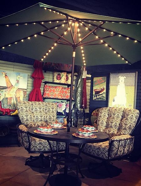 A patio with a table and chairs under an umbrella at night.