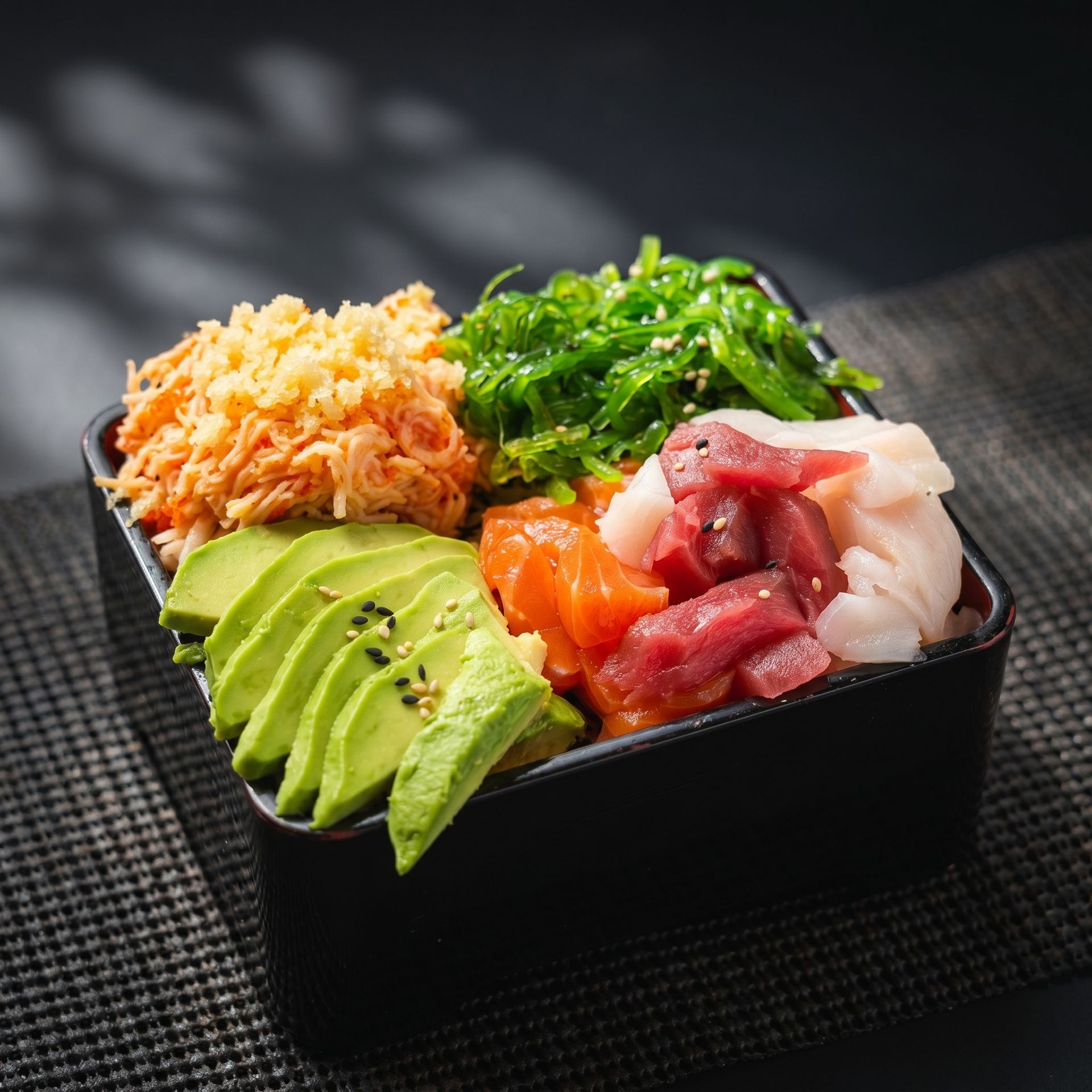 Sushi bowl with avocado slices, salmon, tuna, and greens on a dark table
