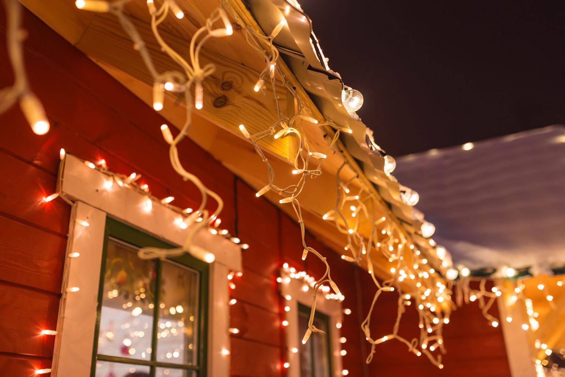 String lights draped along a red house roof and eaves at dusk