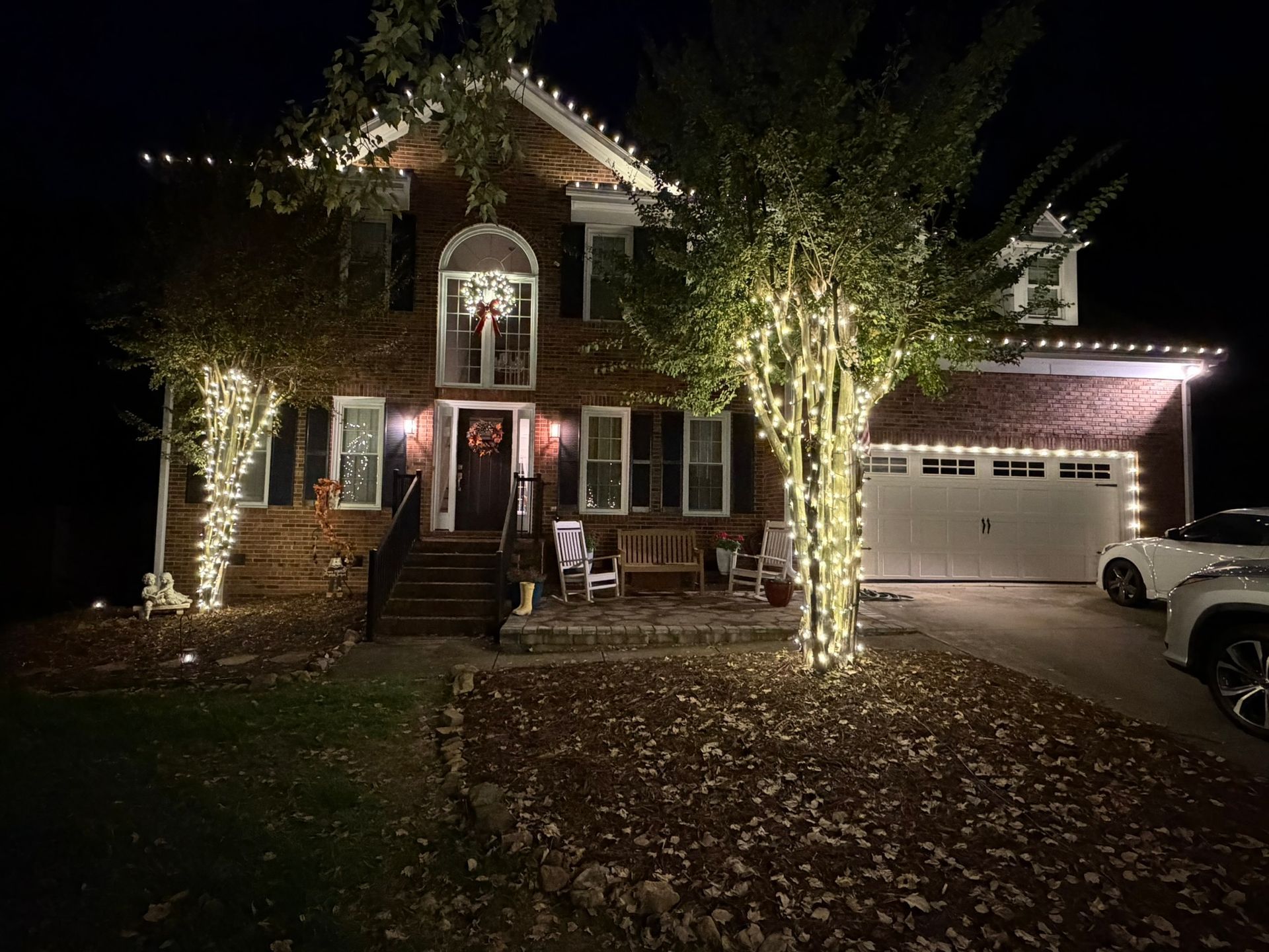 Retrofitted Christmas lights along a roofline, crape myrtle trees and a large prelit wreath and red bow mounted on the window on a home in Concord