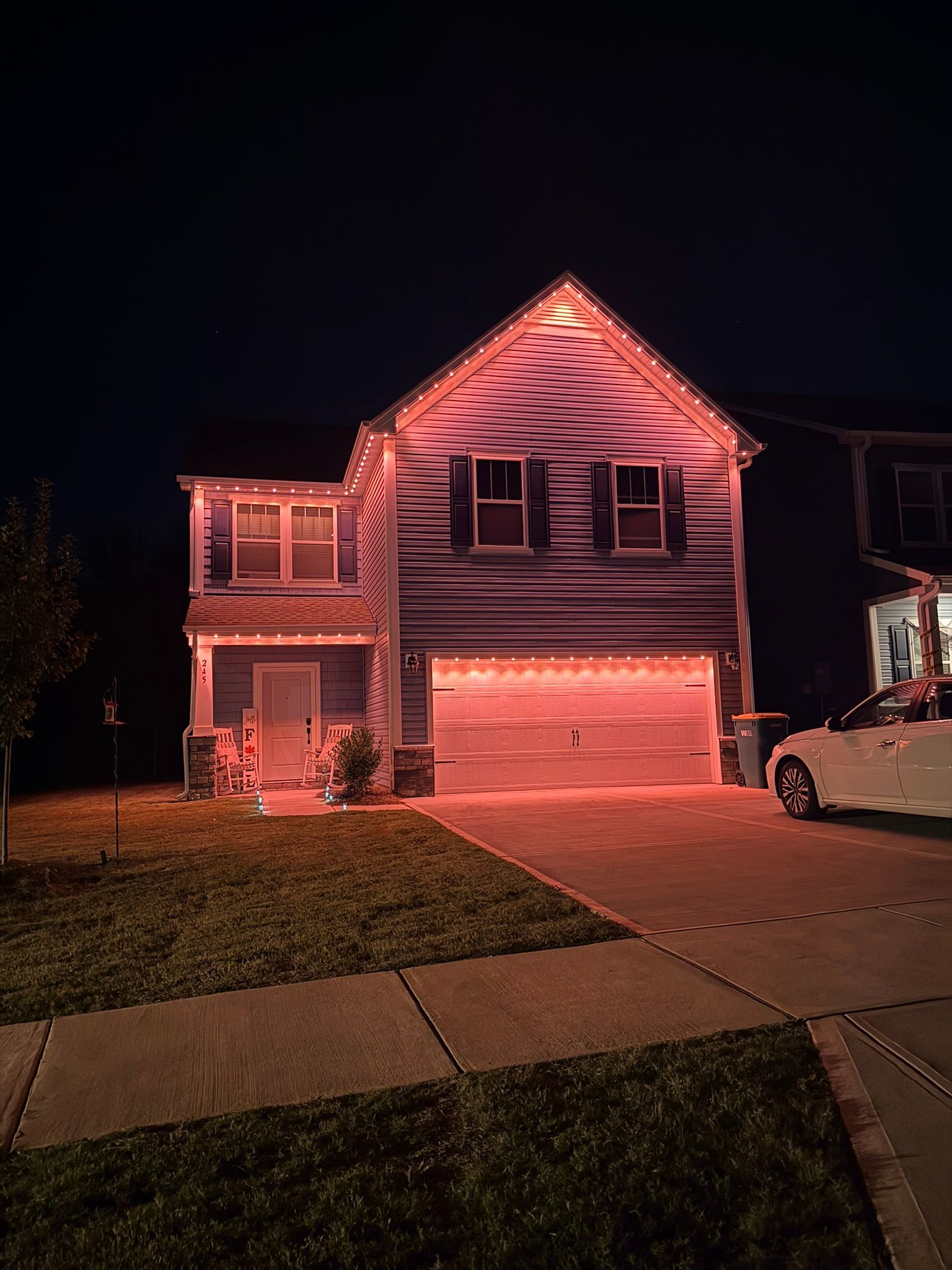 Two-story suburban house lit pink at night, with a garage and a car in the driveway.