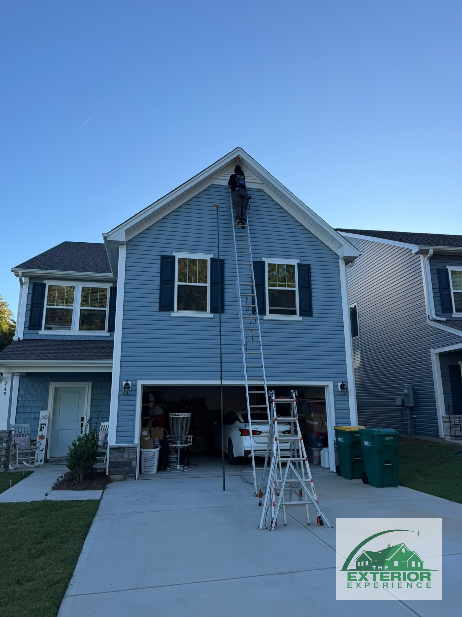 Two-story blue house with workers on scaffolding and ladders during exterior repair.