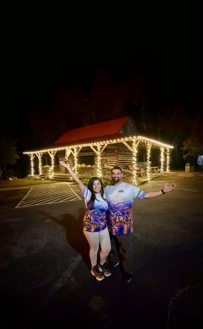 Two people posing at night in front of a lit building with string lights and a red roof