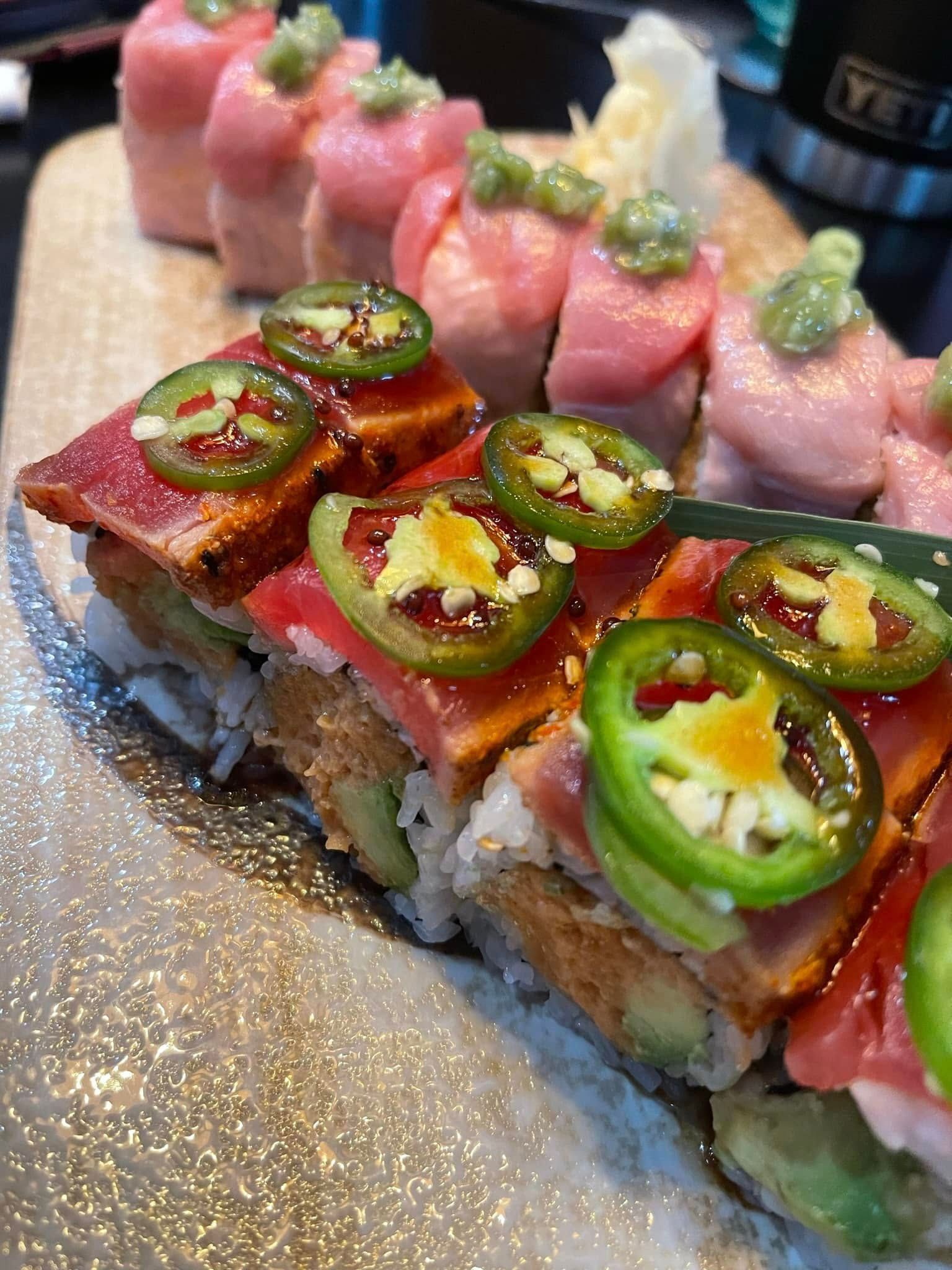 Sushi rolls topped with tuna and jalapeños, presented on a wooden board.