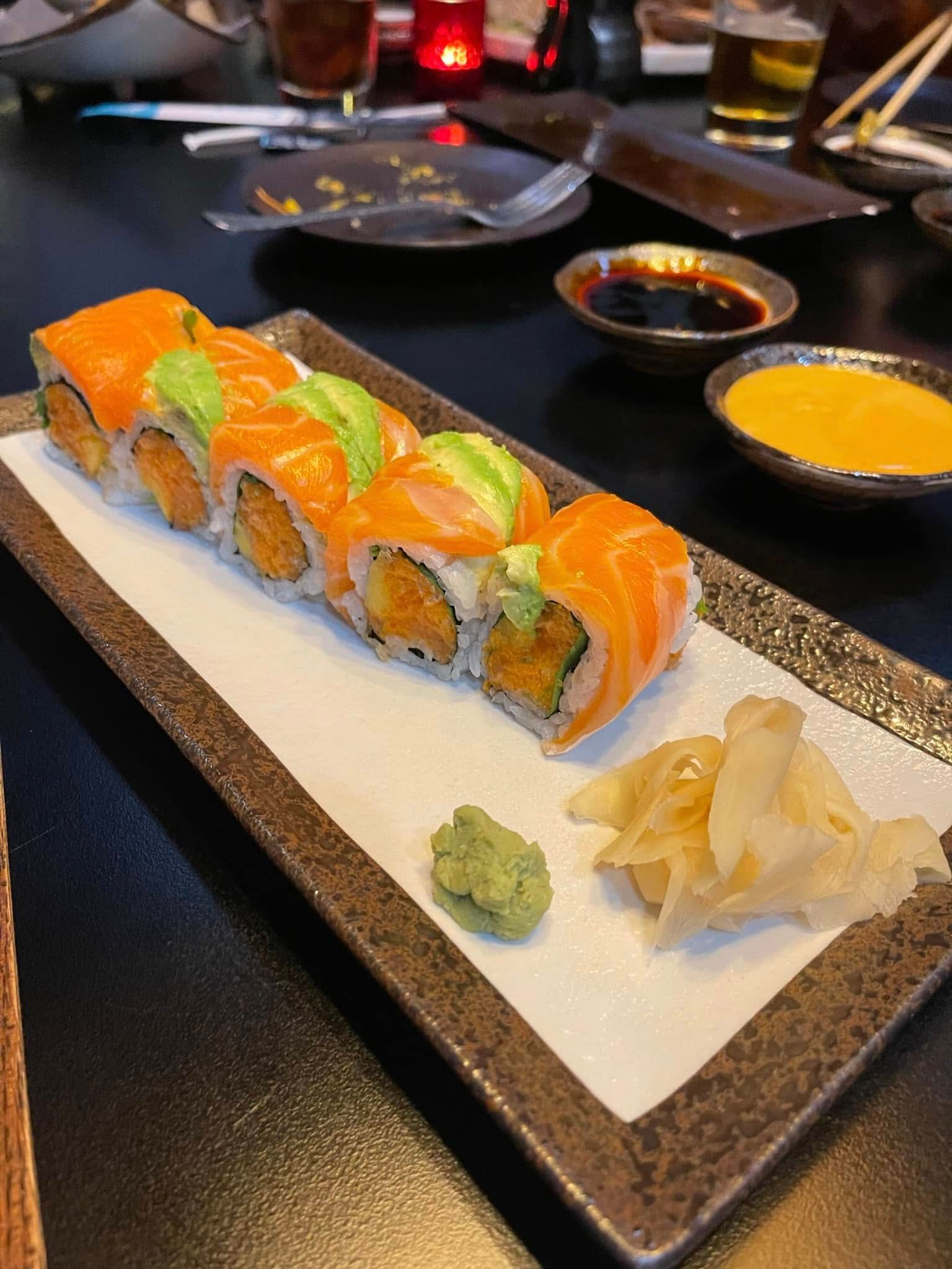 Sushi roll with salmon, avocado, sauces, and wasabi on a rectangular plate.