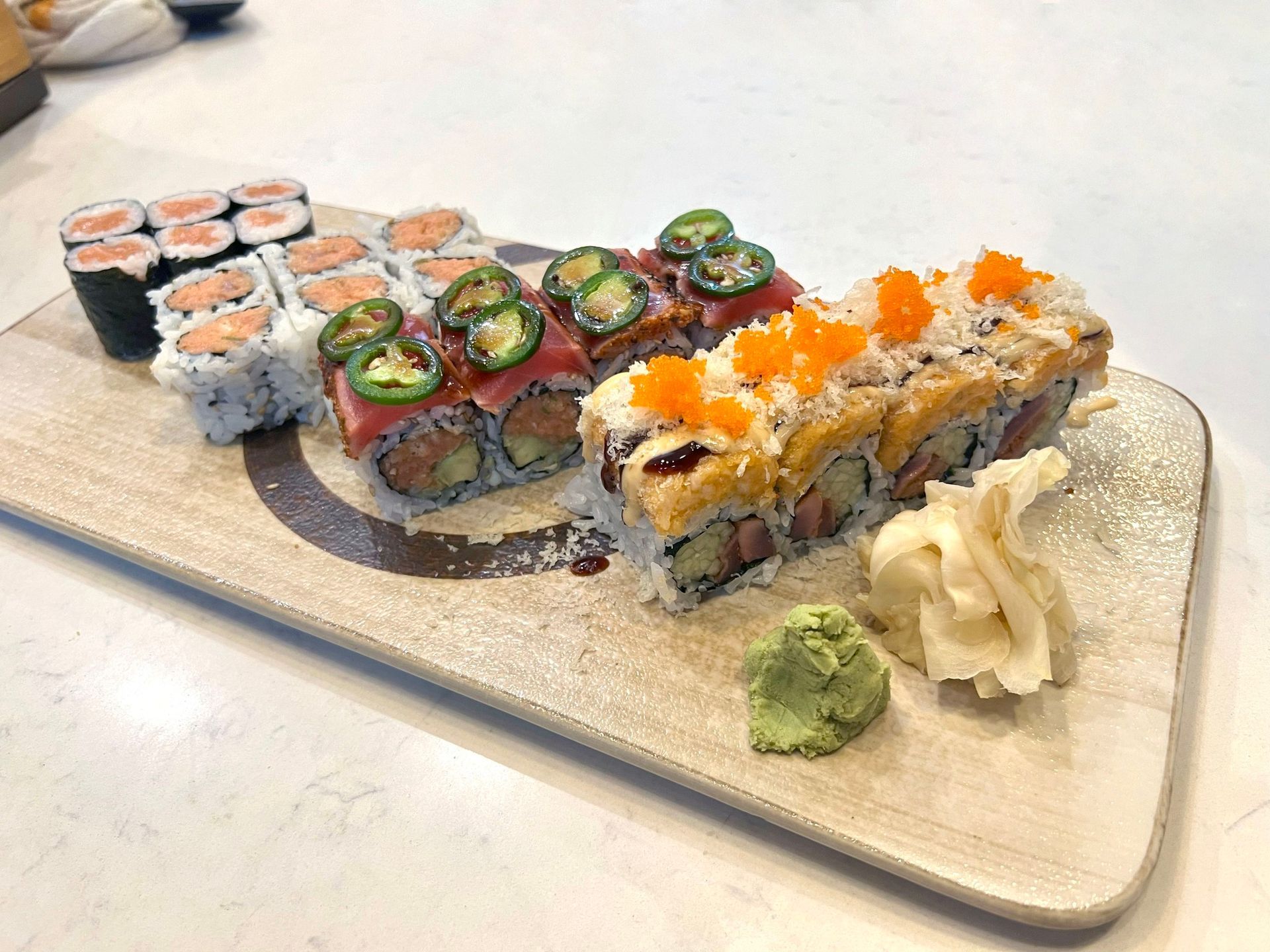 Sushi rolls on a rectangular plate with wasabi and pickled ginger.
