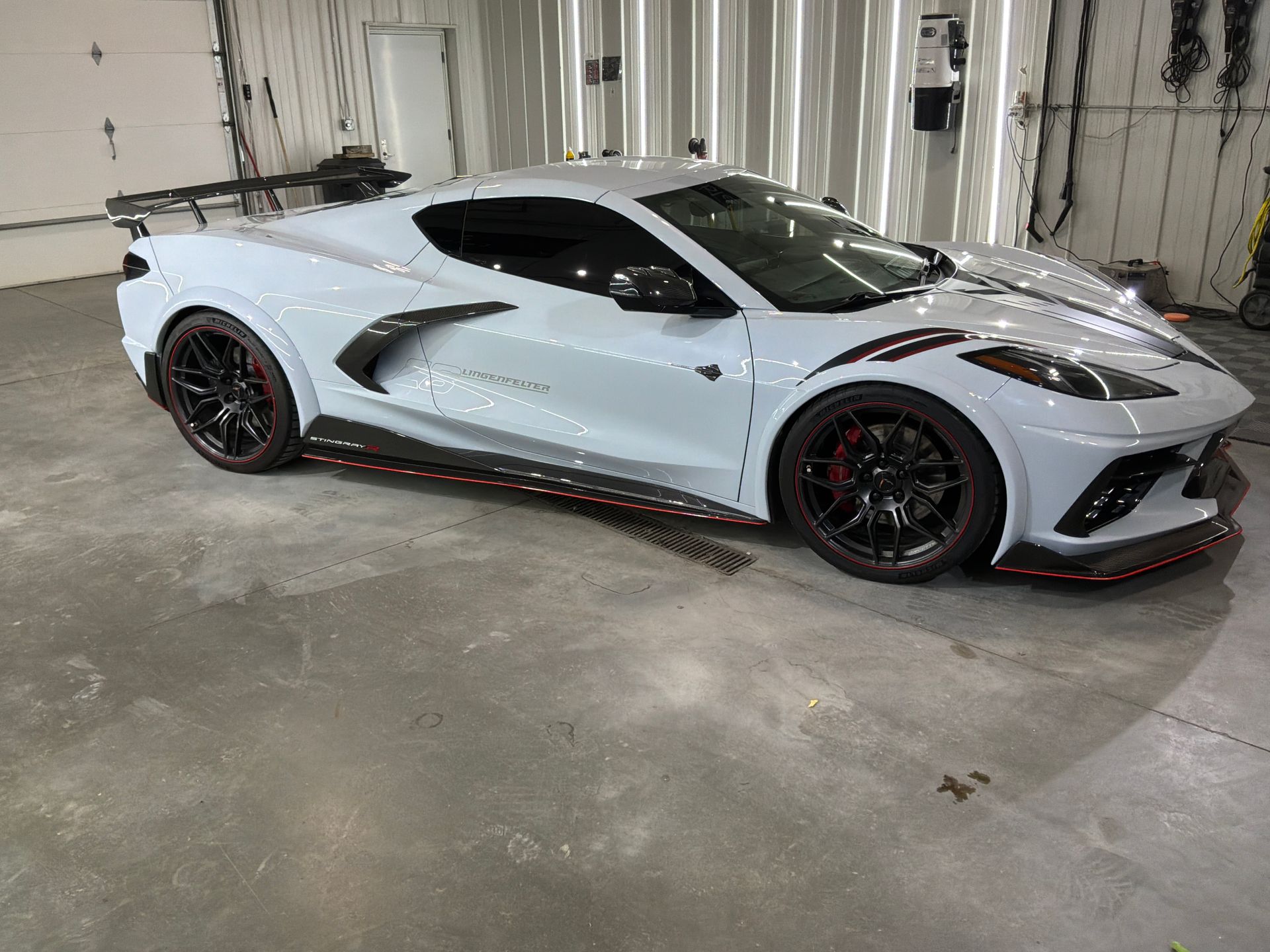 Silver sports car parked indoors in a garage, side view with black wheels and red accents