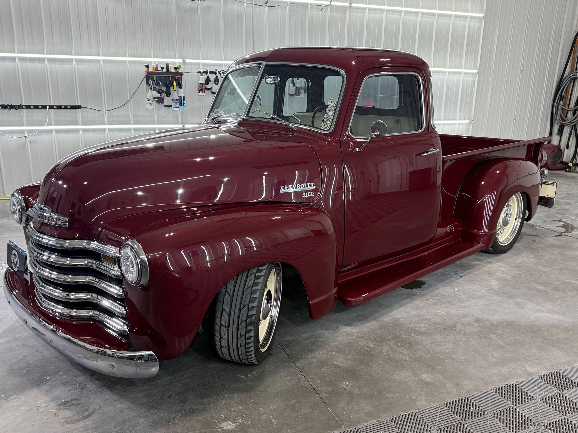 A shiny, deep maroon vintage Chevrolet pickup truck with chrome accents parked indoors on a concrete floor.